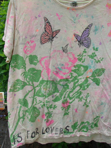 Magnolia Pearl Cotton Jersey Boyfriend Tee ... Is For Lovers OSFA, featuring a watercolor-style floral motif with butterflies, faint pastel splashes, and the phrase “IS FOR LOVERS” along the hem.