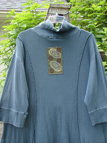 Barclay Patched Thermal Quad Drop Pocket Tunic Dress in Blue Tealen, featuring a double-layered turtleneck, whimsical nature-themed patches, and four drop pockets, displayed on a hanger.