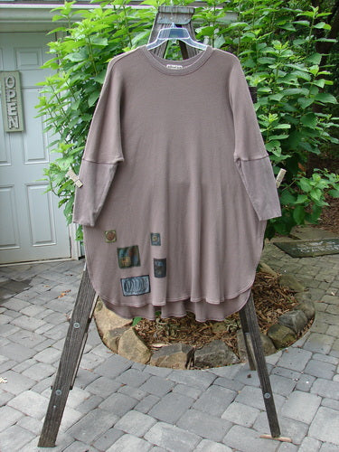 Barclay Patched Thermal Revival Top Abstraction Sand OSFA hanging on a clothes rack, showcasing its unique round hemline, extreme A-line shape, ribbed lower sleeves, and distinctive abstract patches.