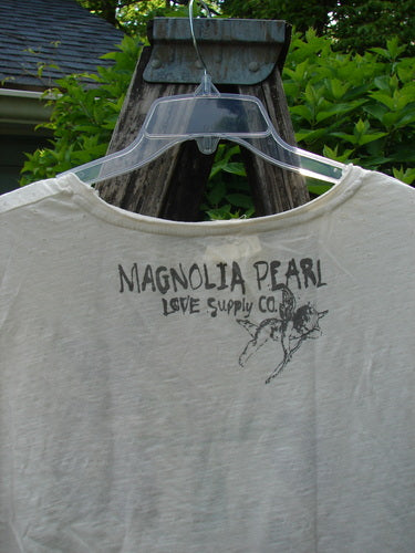 Magnolia Pearl Cotton Jersey Boyfriend Tee Iris Garden OSFA, featuring the “MAGNOLIA PEARL LOVE SUPPLY CO.” print and a magnolia blossom on the back, hangs outdoors, showcasing its lightweight, drapey design.