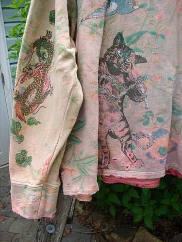 Magnolia Pearl Fleece Lucky Anna Glitter Sweatshirt Marais OSFA draped outdoors, showcasing a dragon print on one sleeve and a playful cat with birds and flowers on the other, featuring tattered edges.