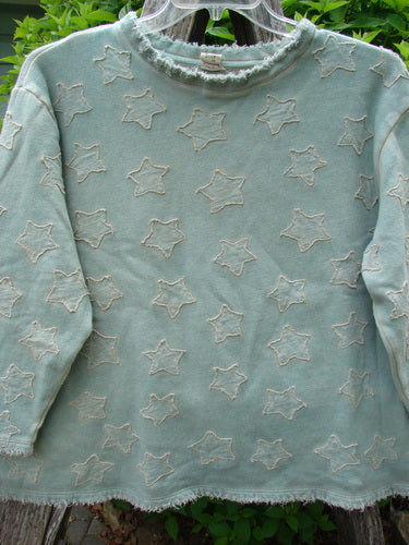 Magnolia Pearl Fleece Applique Little Star Hermosa Sweatshirt Garden Sage OSFA features a light mint-green pullover with frayed edges, cream star outlines, and a roughed-up neckline, hanging on a clear hanger.