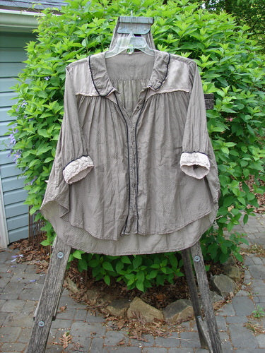 Magnolia Pearl Silk Cotton Poet's Billow Blouse in Blue Grey Shore draped on a wooden ladder outdoors, showcasing its ruffled collar, button front, and roll-tab sleeves against a leafy backdrop.