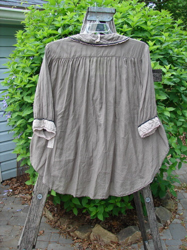 Magnolia Pearl Silk Cotton Poet's Billow Blouse in Blue Grey Shore hangs on a wooden stepladder, showcasing its rounded laced collar, billowy sleeves, and polka dot backdrop against leafy shrubs.