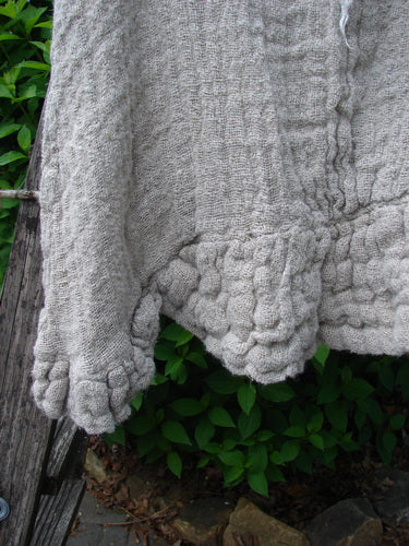 Magnolia Pearl Fisherman's Weave Ribbon Neck Top in Flaxen, hand-knitted textile draped outdoors, featuring a springy square basket weave, sweet neckline snaps, and weighted ruffles along the scalloped hem.
