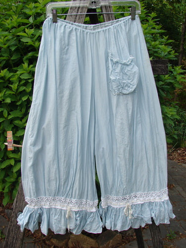 Magnolia Pearl Silk Voile Window Lace Ruffle Pocket Bloomer Sky OSFA, featuring knee-length, loose-fitting design with lace-trimmed ruffles, elastic waistband, and a side patch pocket, hanging outdoors against green shrubbery.