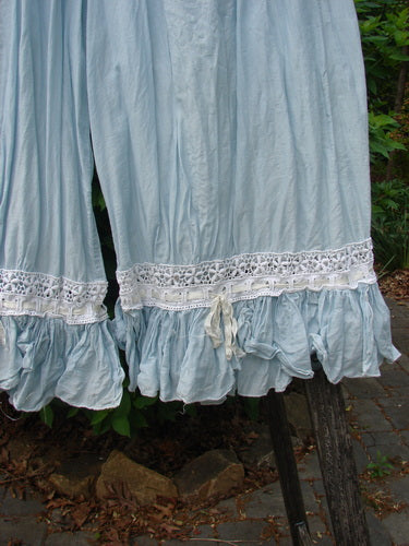Close-up of Magnolia Pearl Silk Voile Window Lace Ruffle Pocket Bloomer Sky OSFA, showcasing light blue ruffled hem with white lace trim and gathered ruffle, hanging outdoors.