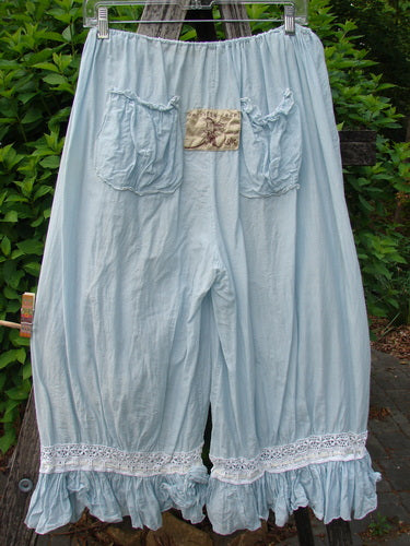 Magnolia Pearl Silk Voile Window Lace Ruffle Pocket Bloomer Sky OSFA features knee-length pantaloons with elastic waistband, gathered front pockets, and ruffled, lace-trimmed hems, hanging outdoors against lush greenery.
