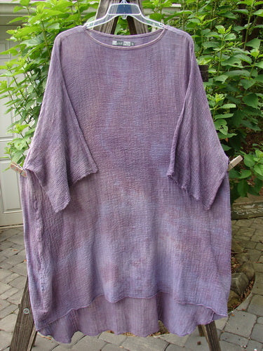 Barclay Gauze Ana Tunic Dress in Unpainted Mottled Lavender Rain displayed on a clothes rack, featuring a slightly shallow rounded neckline, wide three-quarter sleeves, and a varying hemline.