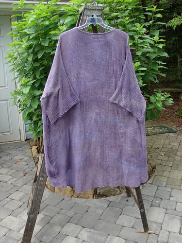 Barclay Gauze Ana Tunic Dress Unpainted Mottled Lavender Rain OSFA displayed on a wooden rack, showcasing its generous, flowing design and wide three-quarter length sleeves with lower frays.