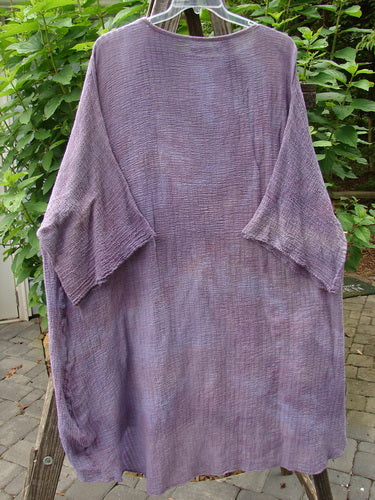 Barclay Gauze Ana Tunic Dress Unpainted Mottled Lavender Rain OSFA on a clothes rack, showcasing its wide three-quarter sleeves, shallow rounded neckline, and varying hemline.