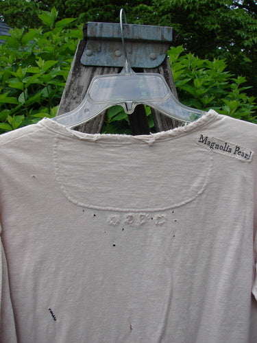Magnolia Cotton Jersey Tobacco Picker's Henley Tee Tea Stain OSFA hanging on a wooden post, featuring a drapey feel, tattered edges, and pearly buttons, capturing vintage Blue Fish style.