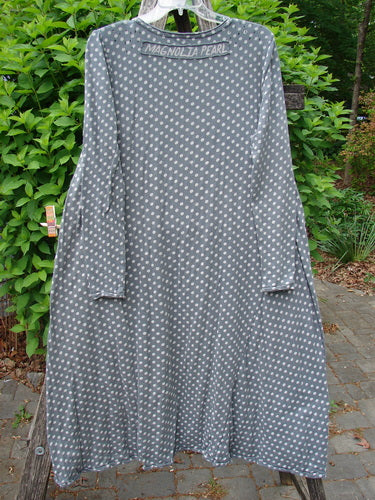 Magnolia Pearl Cotton Dylan Dress Ozzy Tiny Continuous Polka OSFA hangs on a clear hanger, showcasing its long sleeves, full skirt, distressed detailing, and distinctive polka-dot pattern against a green backdrop.