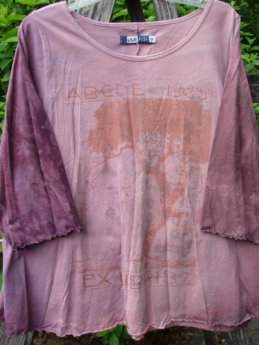 Barclay Three Quarter Sleeved Cafe Tee Alphabet Mottled Peony Size 0, features a loose fit with darker 3/4 sleeves, a distressed graphic with faint lettering, and a tree image, hanging against greenery.