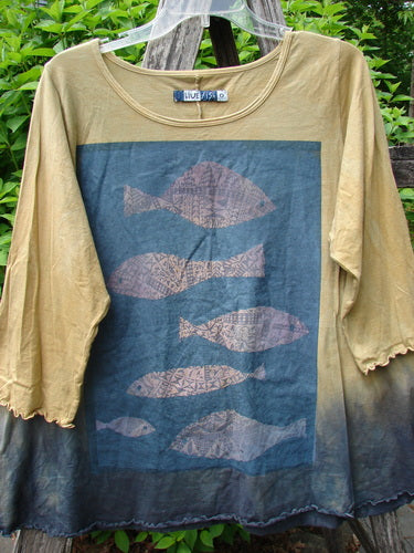 Barclay Three Quarter Sleeved Cafe Tee Sea of Fish Mottled Mustard Size 0 displayed against a rustic backdrop, showcasing muted yellow and navy dip-dye, stylized fish graphics, and unique curly edgings.