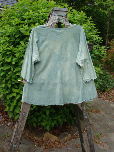 Barclay Three Quarter Sleeved Cafe Tee Owl Forest Mottled Mint Size 0, draped on a wooden stepladder outdoors, showcasing its A-line shape, rounded neckline, and curly edgings in a natural setting.