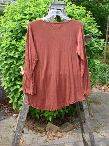Barclay Modal Long Sleeved A Lined Tee in Fall Woods Cassia, draped over a wooden ladder, showcasing its unique A-line shape and ribbed neckline, set against an outdoor backdrop.