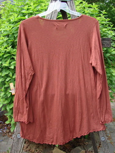 Barclay Modal Long Sleeved A Lined Tee in Fall Woods Cassia, size 0, is displayed with a lightweight, rust-brown fabric, featuring a lettuce edge hem and cuffs, against green foliage.