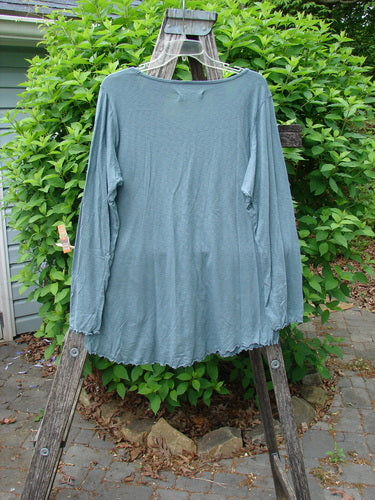 Barclay Modal Long Sleeved A Lined Tee Promo Field Dusky Sky Size 0, draped on a hanger over a wooden stepladder, showcases its unique neckline and A-line shape against a natural outdoor backdrop.