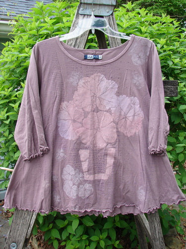Barclay Crop A Lined Cafe Tee in Potted Floral City Moonlight Mauve, displayed on a plastic hanger over a wooden ladder, features three-quarter sleeves, a rounded neckline, and intricate floral motifs.