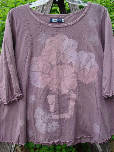 Barclay Crop A Lined Cafe Tee in muted mauve, featuring a faded stenciled flower-in-a-pot motif, hanging on a plastic hanger outdoors.