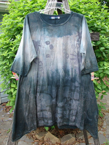 Barclay Wander Tunic Tee Rain Star Mottled Night Size 0, featuring an abstract pattern, elbow-length sleeves, draped hem, and rounded neckline, hanging on a clear hanger against a garden backdrop.