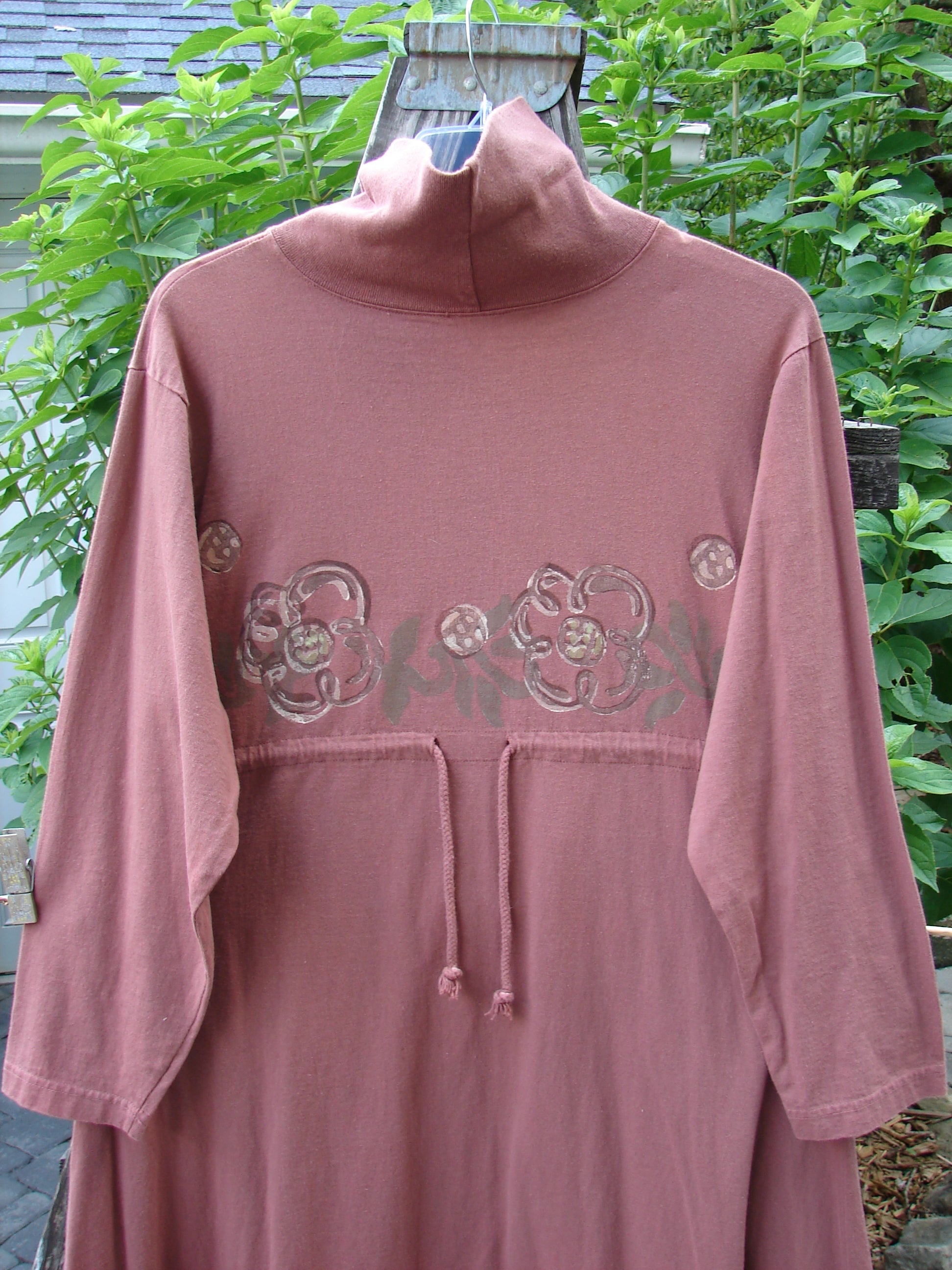 Alt text: 1995 Omega Dress Celestial Garden Altered Clove Size 1, featuring a pink shirt with a flower design, heavy ribbed turtleneck, drop shoulders, and drawcord backline.