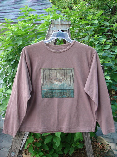 1994 PMU Patched Long Sleeved Tee Rosewood Size 1 on a hanger, showcasing its rolled neckline, significant patches, and cozy long sleeves, displayed against an outdoor background with plants.