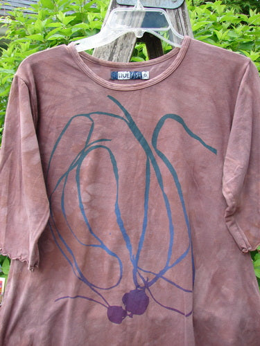 Barclay Cotton Lycra Three Quarter Sleeved A Line Tee Roots Mottled Clay Size 0, featuring a scoop neck, abstract teal and deep purple graphic, hanging on a plastic hanger amidst green foliage.