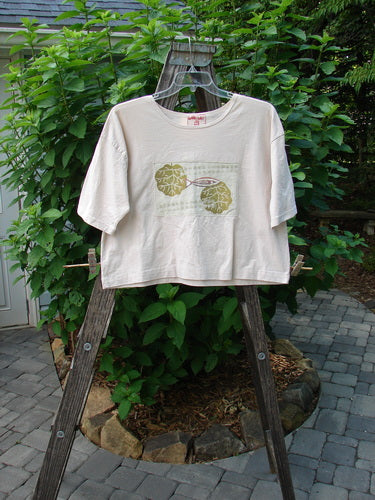 Barclay PMU Patched Short Sleeved Crop Tee Fish Creme Size 0 displayed on a wooden ladder, showcasing its hand-stitched crop length, square boxy shape, and single fish patch design.