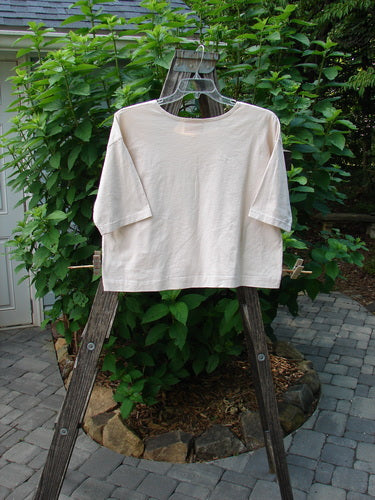 Barclay PMU Patched Short Sleeved Crop Tee Fish Creme Size 0 displayed on a wooden rack, showcasing its square boxy shape, short sleeves, folded neckline, and single fish patch.