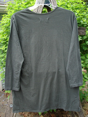 Barclay Long Sleeved Studio Tee Moon Gull Garden Ash Black Size 0, displayed on a clear hanger with a wooden support, set against a backdrop of leafy green shrubs in a garden.