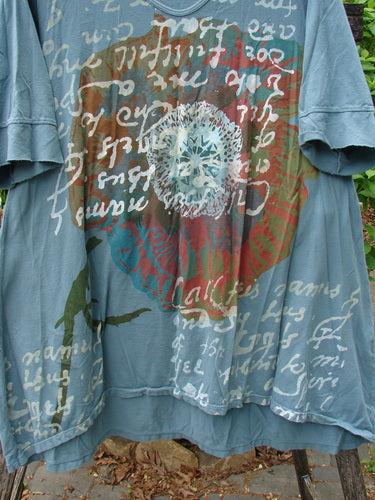 Barclay Three Quarter Sleeved Happiness Tunic Floral Notes Dusty Sky Size 0, features a teal T-shirt with cursive script, central red-olive graphic, abstract shapes, and a unique hemline hanging outdoors.