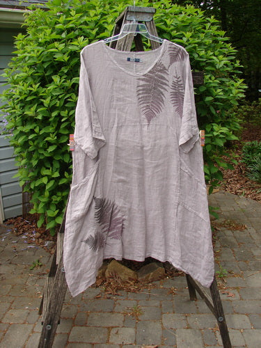 Barclay Linen Wave Pocket Dress Fern Mallow Quartz Size 0, featuring a knee-length design with fern-leaf prints, a rounded neckline, pinched sleeves, and seamless bodice, displayed on a wooden trellis.