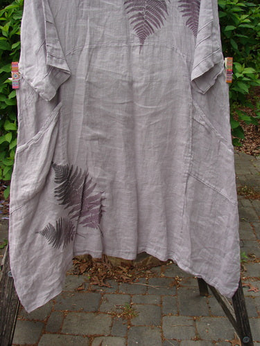 Barclay Linen Wave Pocket Dress Fern Mallow Quartz Size 0, featuring a loose knee-length design with fern prints, oval neckline, and front drop pockets, displayed outdoors with greenery in the background.