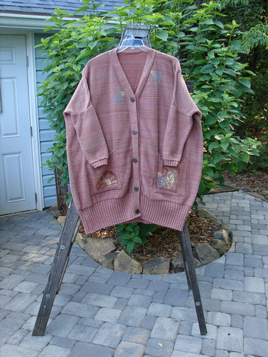 1995 Fireside Cardigan Sweater Single Sprig Marled Brick OSFA displayed on a clothes rack, showcasing its deep neckline, oversized pockets, metal buttons, and ribbed hem and sleeves.