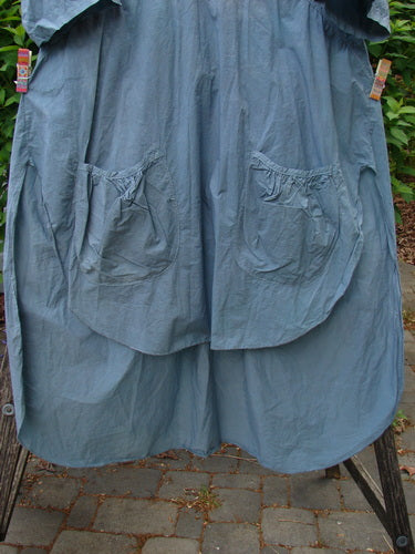 Barclay Percale Key Pocket Hi Low Dress Flower Dish Stream Size 0 displayed outdoors on a drying rack, featuring dual front pockets, wide sleeves, and a unique rounded front and back hemline.