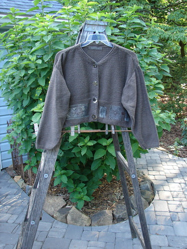 Alt text: 1994 Crop Cardigan Sweater Topiary Humus OSFA on a clothes rack, showcasing its unique dual contrasting knits, stoneware buttons, and cozy longer sleeves.
