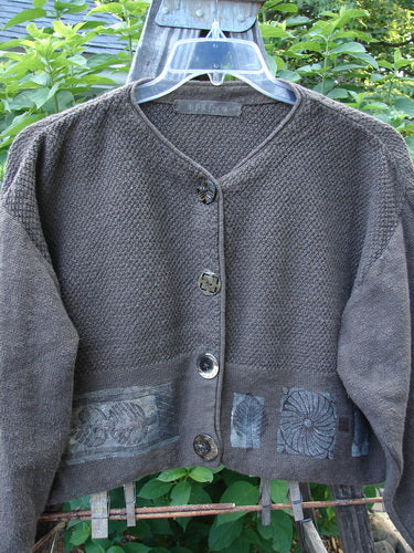 1994 Crop Cardigan Sweater Topiary Humus OSFA displayed on a hanger outdoors, showcasing its variegated hand-dyed texture, stoneware buttons, cozy longer sleeves, and unique topiary theme paint.