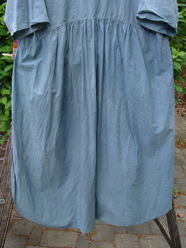 Barclay Percale Key Pocket Hi Low Dress Flower Dish Stream Size 0, featuring a loose fit, gathered waist, distinctive rounded hemline, and dual pockets, displayed outdoors amidst paving stones and greenery.