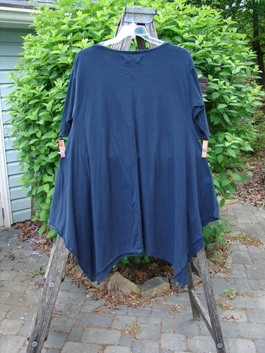 Barclay Origami Tunic Top Night Garden Blue Ink Size 0 displayed on a wooden ladder, showcasing its handkerchief hem, raw edges, and oval neckline against a green outdoor background.