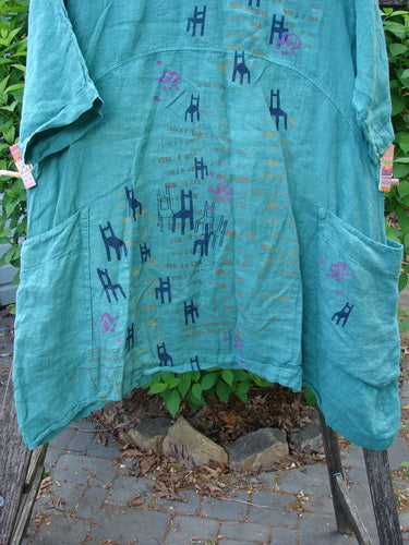 Barclay Linen Side Pocket Urchin Dress Chair Note Jade Size 0 features a textured, teal-green fabric with chair motifs, short sleeves, and large patch pockets, draped over a wooden ladder outdoors.