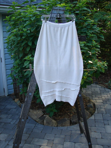 Barclay Thermal Awen Skirt Unpainted Creme Size 0 displayed on a clothes rack, showcasing its unique bell shape, full elastic waistband, and textured diagonal hemline.