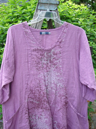 Barclay Linen Posey Dress Tiny Floral Orchid Size 0, with a scooped neckline, three-quarter sleeves, front patch pockets, and a unique floral print, displayed on a hanger amidst greenery.