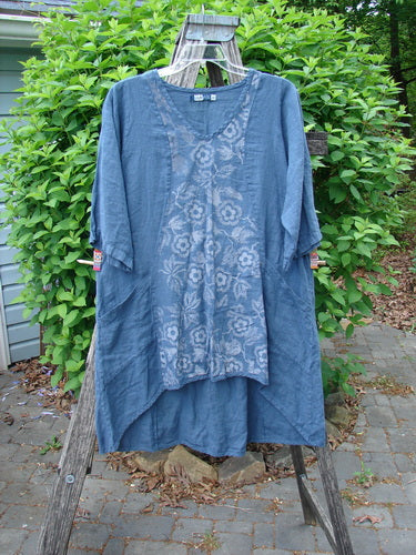Barclay Linen Posey Dress Daisy Ray Blue Echo Size 0, showcasing an oval neckline, elbow-length sleeves, two front pockets, and subtle floral patterns, draped artistically on a wooden ladder outdoors.