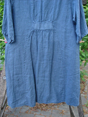 Barclay Linen Posey Dress Daisy Ray Blue Echo Size 0, draped on a wooden bench outdoors, features an oval neckline, flowy figure-eight shape, and exterior drop front pockets.