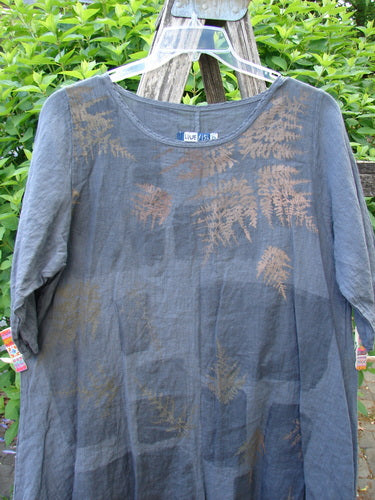 Barclay Linen Lucida Top Metallic Fern Blue Storm Size 0 displayed on a hanger with a round neckline and mid-length sleeves, featuring a muted fern-leaf print, hung on a rustic ladder.