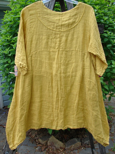 Barclay Gauze Linen Cross Over Dress Unpainted Sunshine Spice Size 1; a loose-fitting, mustard-yellow tunic with a scooped neckline, elbow-length sleeves, and A-line swing shape, hanging outdoors amid foliage.
