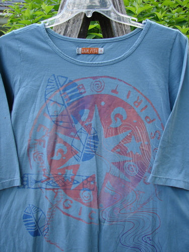 Barclay Three Quarter Sleeved Tee Metallic Belief Spirit Magic Sky Blue Size 1, featuring a slate-blue tone with a large red graphic, hangs outdoors with green foliage in the background, showcasing its unique design.