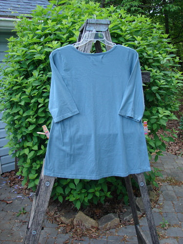 Barclay Three Quarter Sleeved Tee Metallic Belief Spirit Magic Sky Blue Size 1 displayed on a weathered ladder, showcasing its A-line shape, rounded neckline, and flattened edges in an outdoor setting.